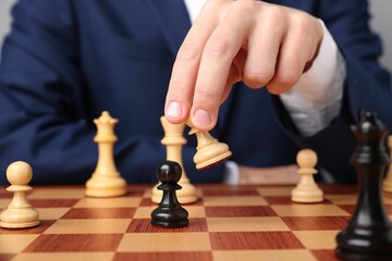 Businessman playing chess on chessboard against light grey background, closeup. Competition concept