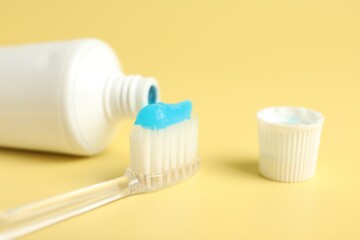 Toothbrush with toothpaste and tube on yellow background, closeup