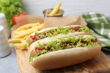 Tasty hot dogs with lettuce, ketchup and potato fries on light grey table, closeup