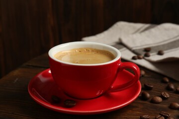 Red cup with coffee and roasted beans on wooden table, closeup