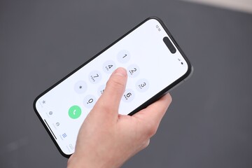 Woman dialing number on smartphone against blurred grey background, closeup