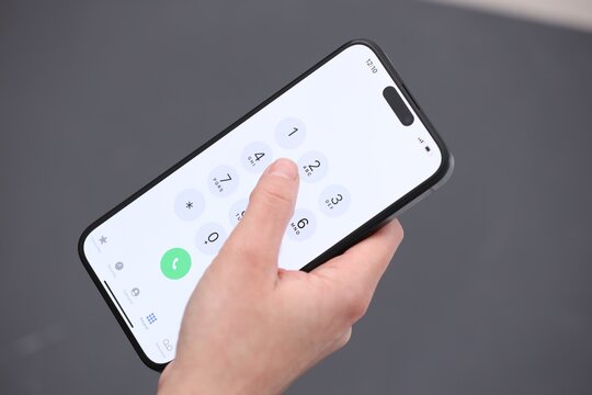 Woman dialing number on smartphone against blurred grey background, closeup