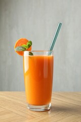 Fresh carrot juice in glass on wooden table against gray background
