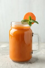 Fresh carrot juice and mint in mason jar on gray textured table