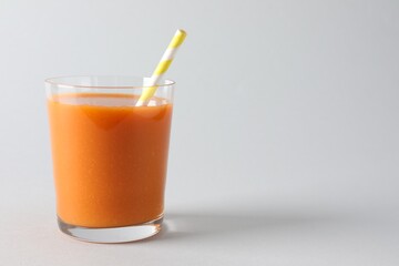 Fresh carrot smoothie in glass on light grey background, closeup. Space for text