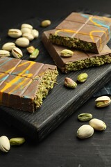 Pieces of Dubai chocolate bars with pistachios and knafeh on black wooden table, closeup