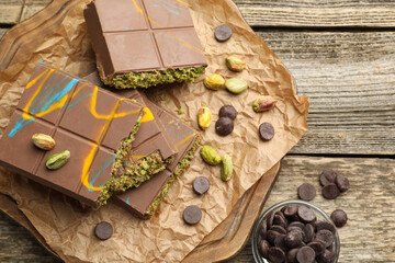Pieces of Dubai chocolate bars with pistachios, knafeh and cacao chips on wooden table, flat lay