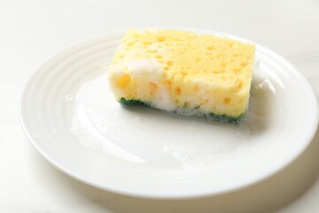 Yellow sponge with foam and plate on white table, closeup