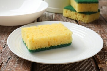 Yellow sponges and dishware on wooden table, closeup