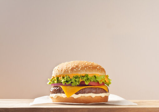 Delicious cheeseburger with lettuce, tomato, and onion on a wooden table