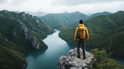 Fototapeta premium Adventurer in Yellow Jacket Stands on Rock Overlooking Serene Mountain Lake and Lush Green Valley Landscape