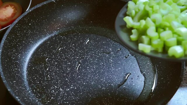 Food preparation. A cook puts chopped celery stalks in a pan for frying. Slow motion footage.