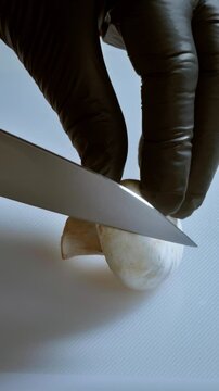 Vertical video, slow motion. Close-up, the chef cut champignon mushrooms into slices on a kichen board.