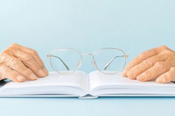 Elderly Hands Holding Open Guidebook with Glasses A Study in Senior Literacy and Technology