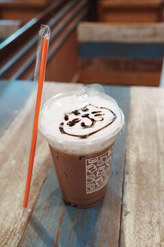 Delicious iced coffee topped with cream and chocolate drizzle on wooden table