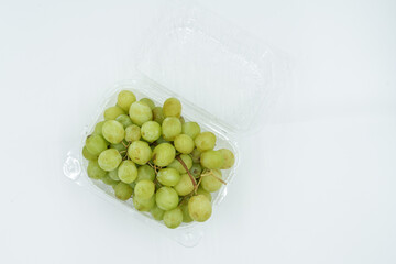 Fresh green grapes in clear plastic container on white background