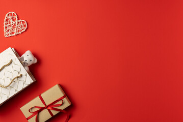 Red background with bear peeking out of gift bag, gift box and heart. Flat lay, top view. Copy space