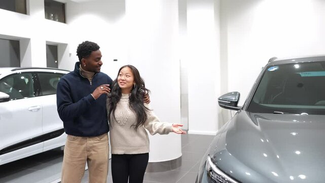 Young couple examines a new car in a dealership showroom, discussing its features in slow motion