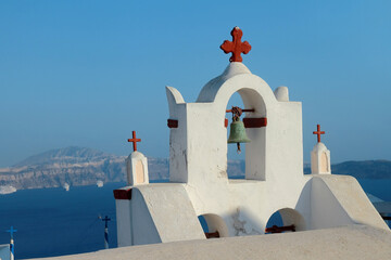 An ancient bell tower with old bells of a Christian church in the Greek style against the background of the blue sea. Caldera of Santorini island.