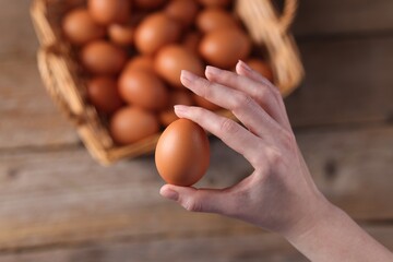 Woman holding raw egg above wooden table, top view