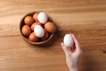 Woman with raw eggs at wooden table, top view