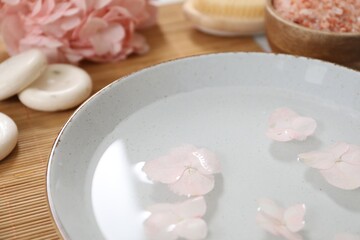 Bowl of water with flowers and different spa supplies on table, closeup