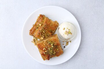 Tasty baklava with chopped nuts and scoop of ice cream on light grey table, top view