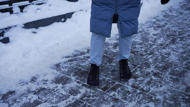 Winter season brings icy sidewalks, requiring careful navigation to avoid slips and falls, as demonstrated by a woman cautiously walking on a frozen path