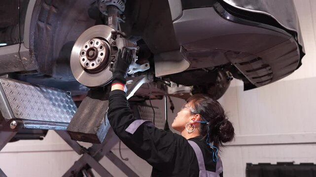Skilled female mechanic working under a lifted car, meticulously repairing brakes in a slow motion sequence