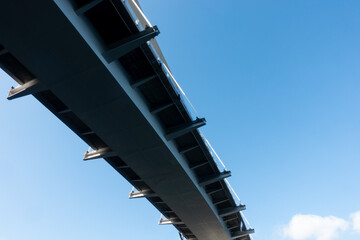 Slightly curved modern steel hanging bridge overpass from below against blue sky in summer for...