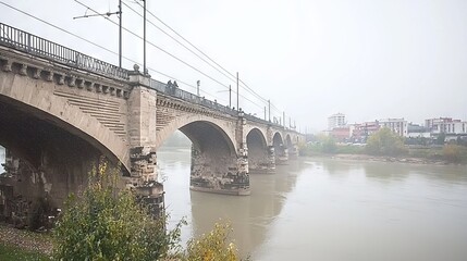 Fototapeta premium A foggy view of a stone bridge over a river with buildings in the background.