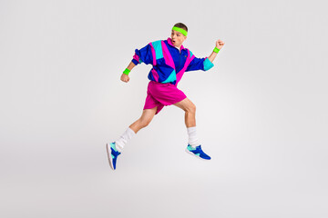 Fototapeta premium Energetic young man in retro style activewear jumping against grey background, full of vitality and joy, showcasing vibrant sports fashion.