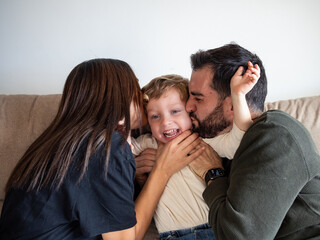 Young couple kiss their son at the same time, sharing a happy moment. Laughter fills the air as they share this joyful experience together.