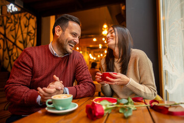 A Caucasian mid adult couple, with backgrounds in professional fields, share joyful moments over coffee in a cozy cafe. Dressed in casual sweaters, they celebrate International Women's Day.
