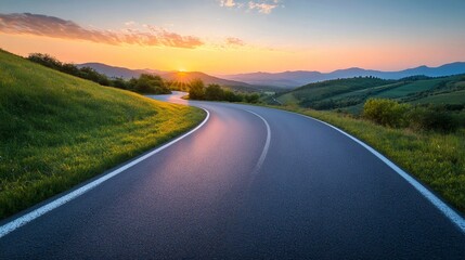 Fototapeta premium Winding road leading into beautiful sunset over green hills