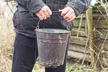 one enameled round old industrial dirty garden with handle empty brown bucket in hands of man in...