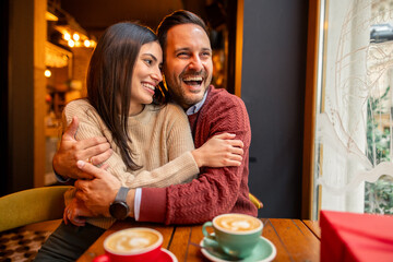 Caucasian mid adult couple, dressed casually, enjoys a romantic Valentine's Day in a cozy cafe. They appear happy and content as they share coffee and embrace.
