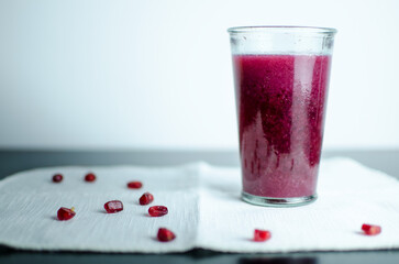 Pomegranate juice in a glass, lose pomegranates on the table, on a homemade unique white crochet napkin, rich colour drink