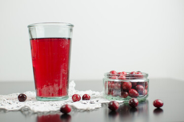 Cranberry juice in a glass, cranberries on the table, on a homemade unique white crochet napkin, Christmas beverage