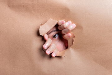 Man looking through a paper hole with his hands pushing the paper aside.