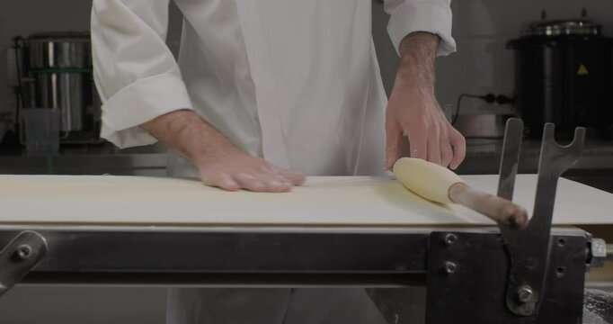 Croissant pasta phyllo dough. Pastry chef rolling dough on a rolling pin, using dough sheeter rolling machine in a bakery kitchen
