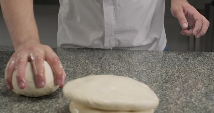 Chef preparing dough for rolling, smashing a piece of dough on a kitchen table with oil hands. Close-up slow motion