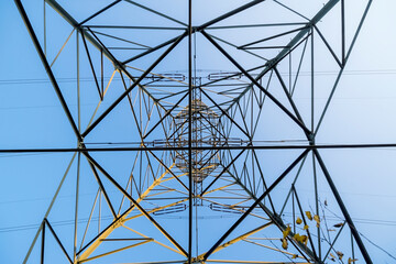 Widok od wewnątrz (w górę - w kierunku szczytu) dużego stalowego słupa elektrycznego. Geometryczne i nieco abstrakcyjne wzory stworzone na tle nieba przez elementy konstrukcyjne dużego stalowego słupa