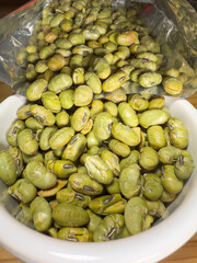 Macro closeup of crunchy, dry roasted Edamame beans snack pouring from a retail packet into a bowl, ready to eat.