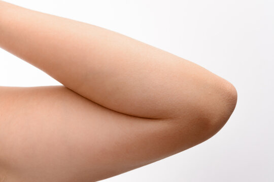 Detailed view of a human arm bent at the elbow, highlighting the skin texture and the joint's structure. The image is set against a plain white backdrop.