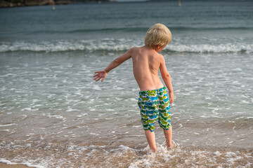 Young boy standing on a sand beach in summer.