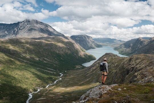 Trekker Standing on Mountain Edge Overlooking Fjord and Norwegian Landscape - Powered by Adobe