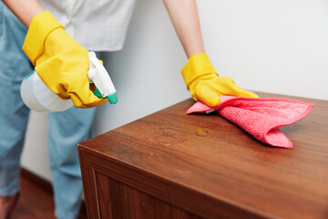 Woman in yellow rubber gloves cleaning wooden table with rag and cleaning solution bottle