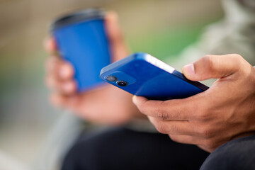 Close-up of hands holding smartphone and coffee cup
