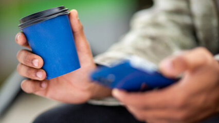 Close-up of hand holding coffee cup with smartphone